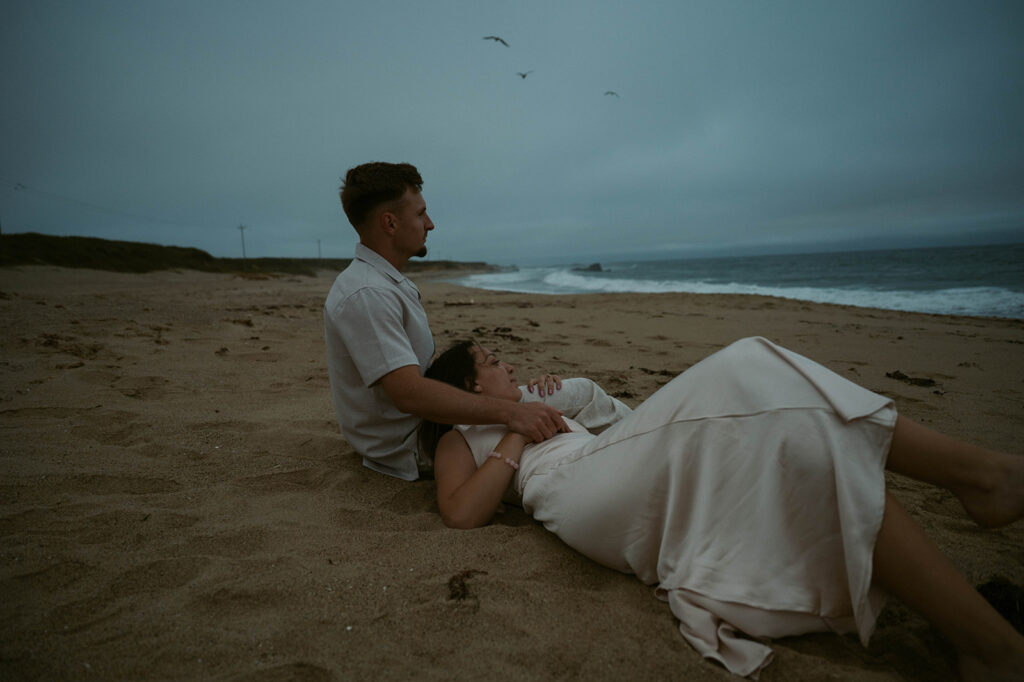 A photo of a couple seated in the sand taken by engagement photographer bay area ca