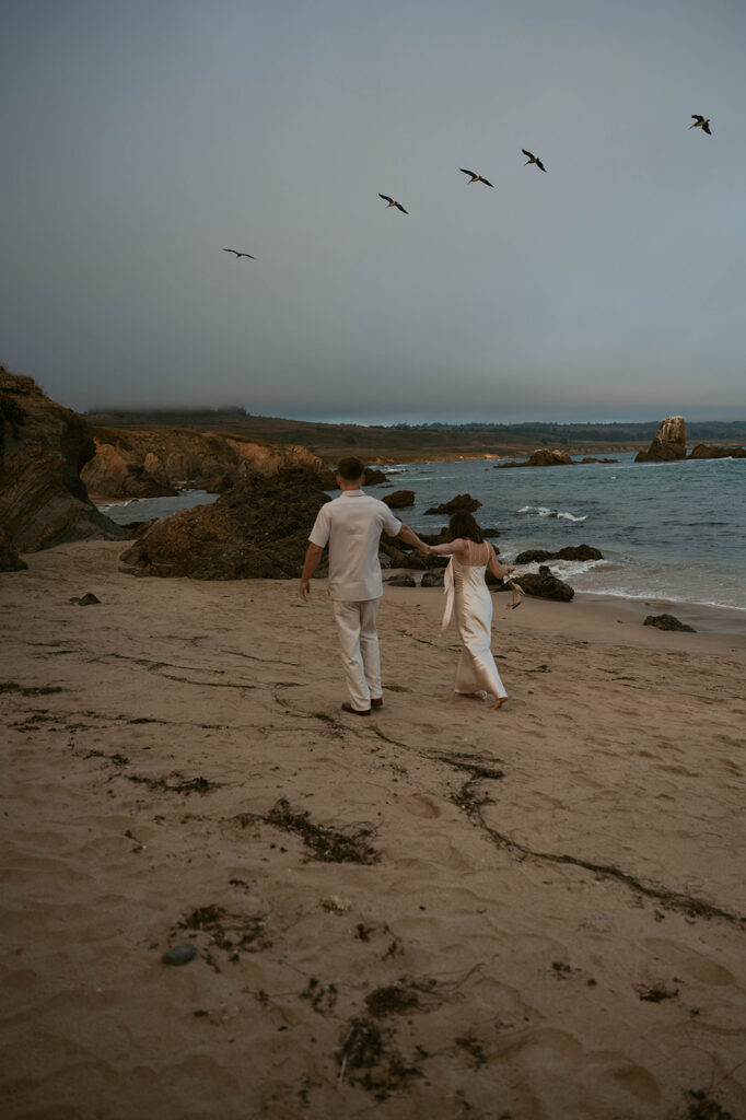 A California couple walks hand in hand along the shoreline of Pigeon Point Lighthouse during their bay area engagement photos
