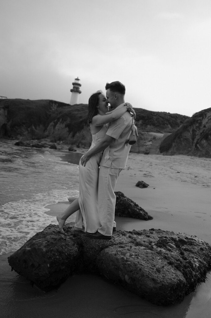 A newly engaged couple embraces along the shoreline at their coastal photoshoot