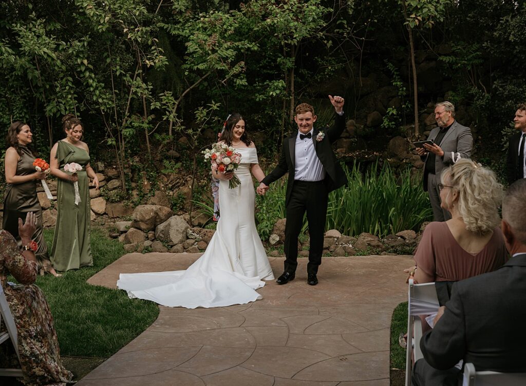 A bride and groom celebrate hand-in-hand as they walk down the aisle following their ceremony at Hanford Garden, a sutter creek wedding venue