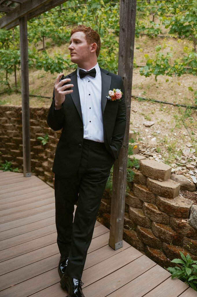 A groom in a black tux  spritzes cologne in a photo taken at Hanford Garden