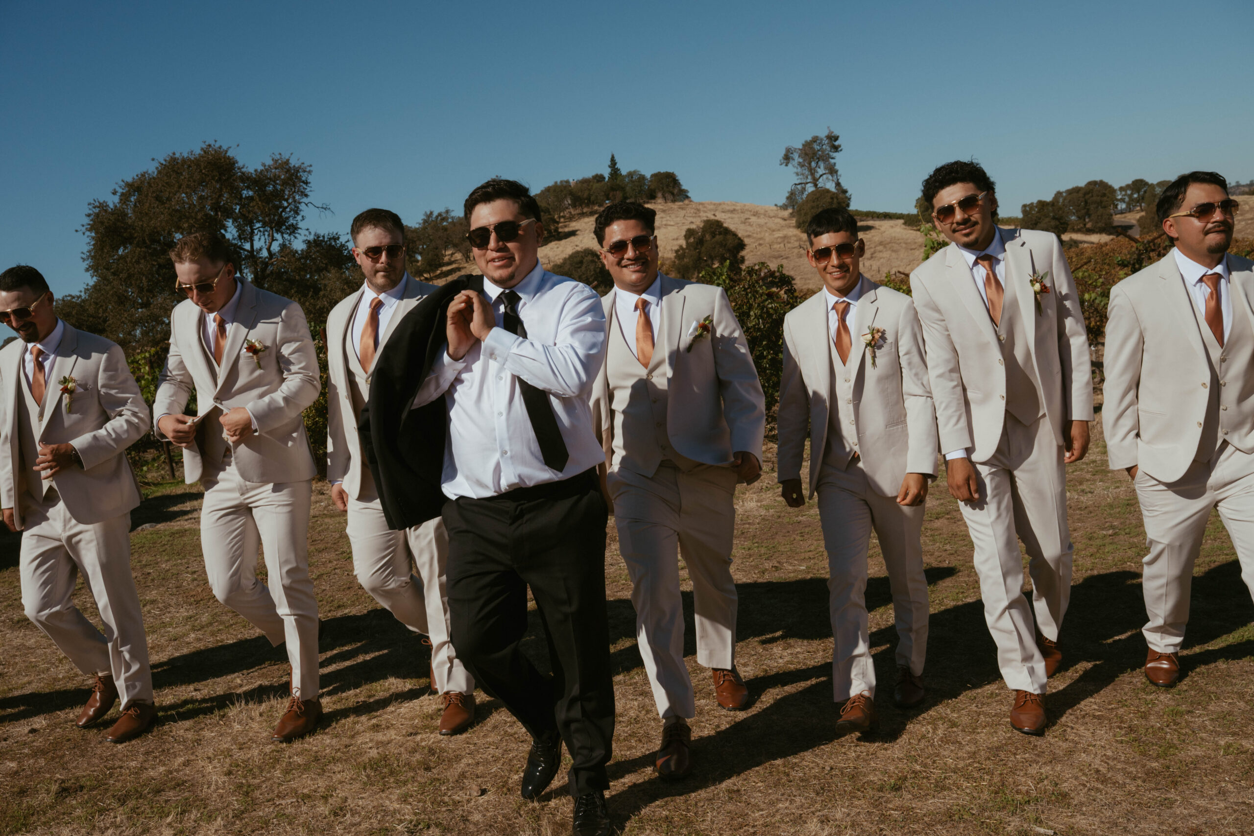 Groom and his groomsmen walk along a field during their portraits at wedding.