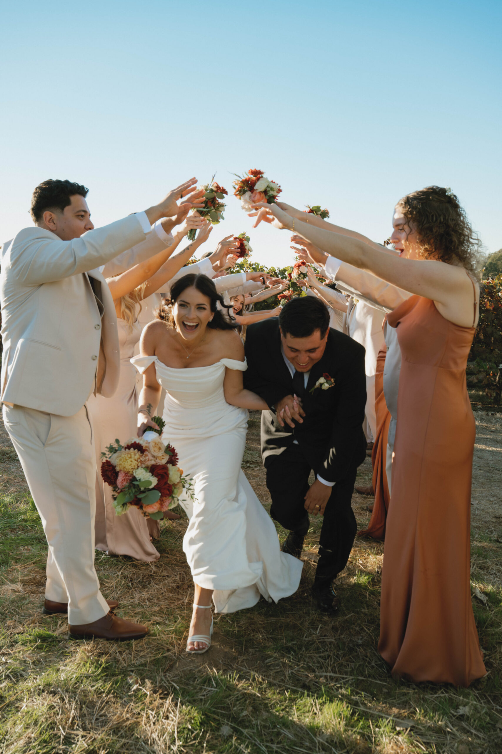 Bridal party makes a floral tunnel over the bride and groom as they run through the tunnel at cazadd cellars