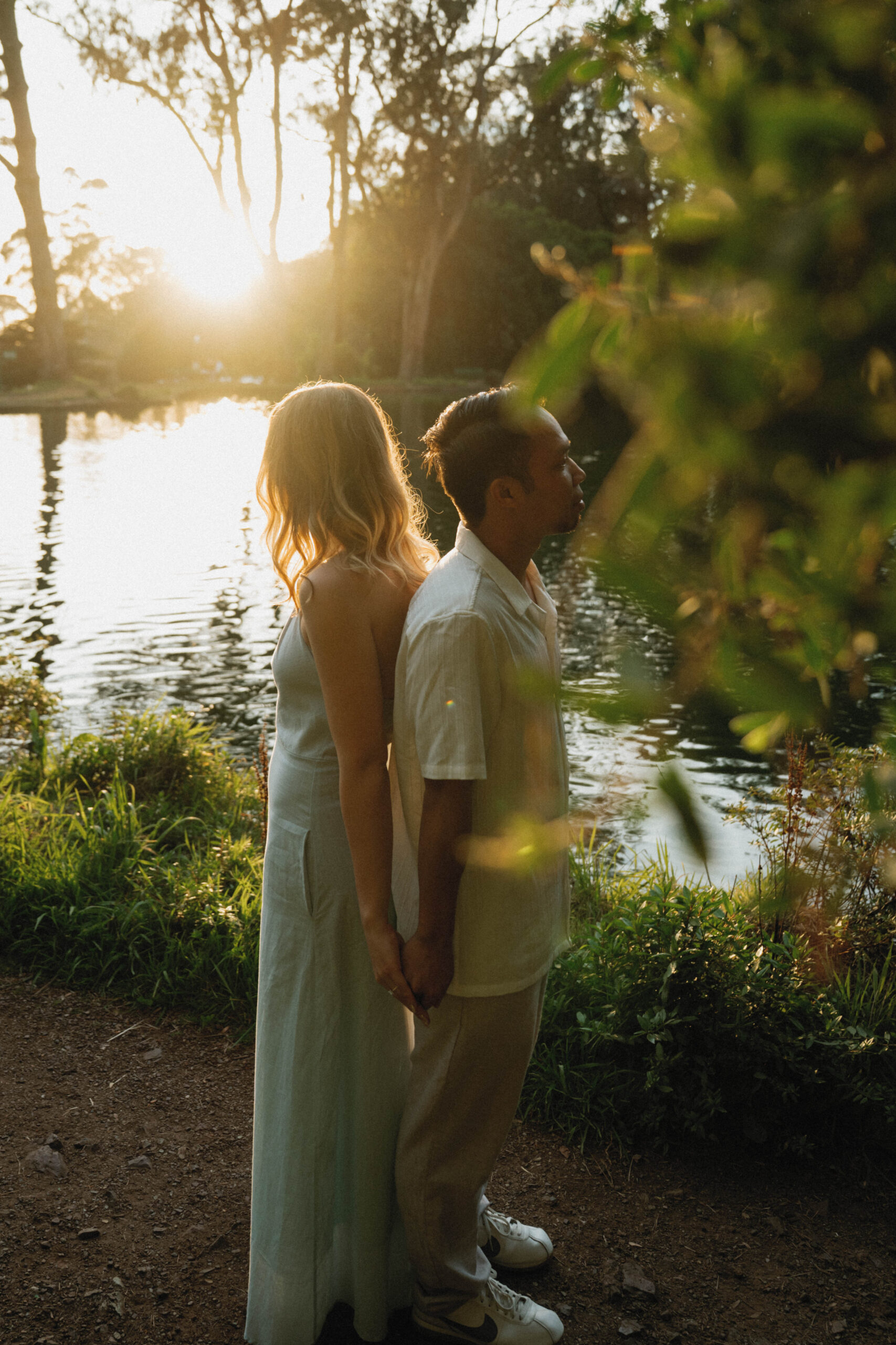 Couples stands back to back holding hands under the golden glow during their engagement photos in San Francisco