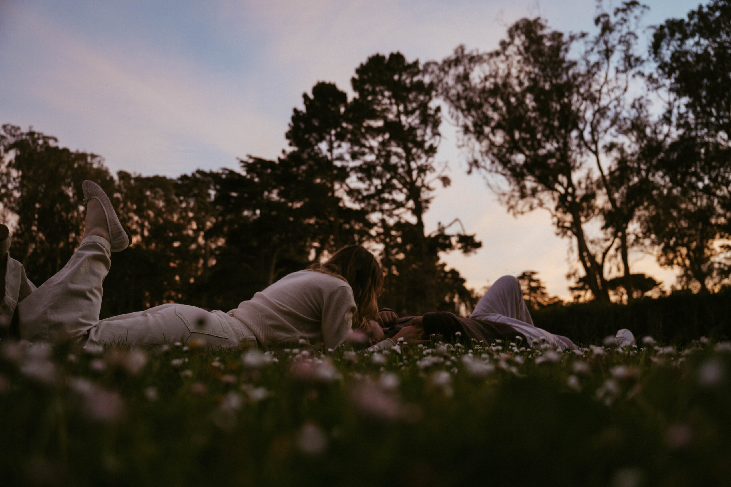 A couple gets cozy on the grass surrounded by daisies while they photograph their engagement in San Francisco